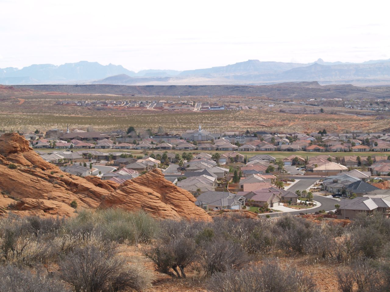 Homeowners insurance Washington City, Utah — view across the 84780 valley with red sandstone bluffs in the foreground, rooftops of Coral Canyon and Washington Fields, and the Pine Valley and Zion mesas on the horizon