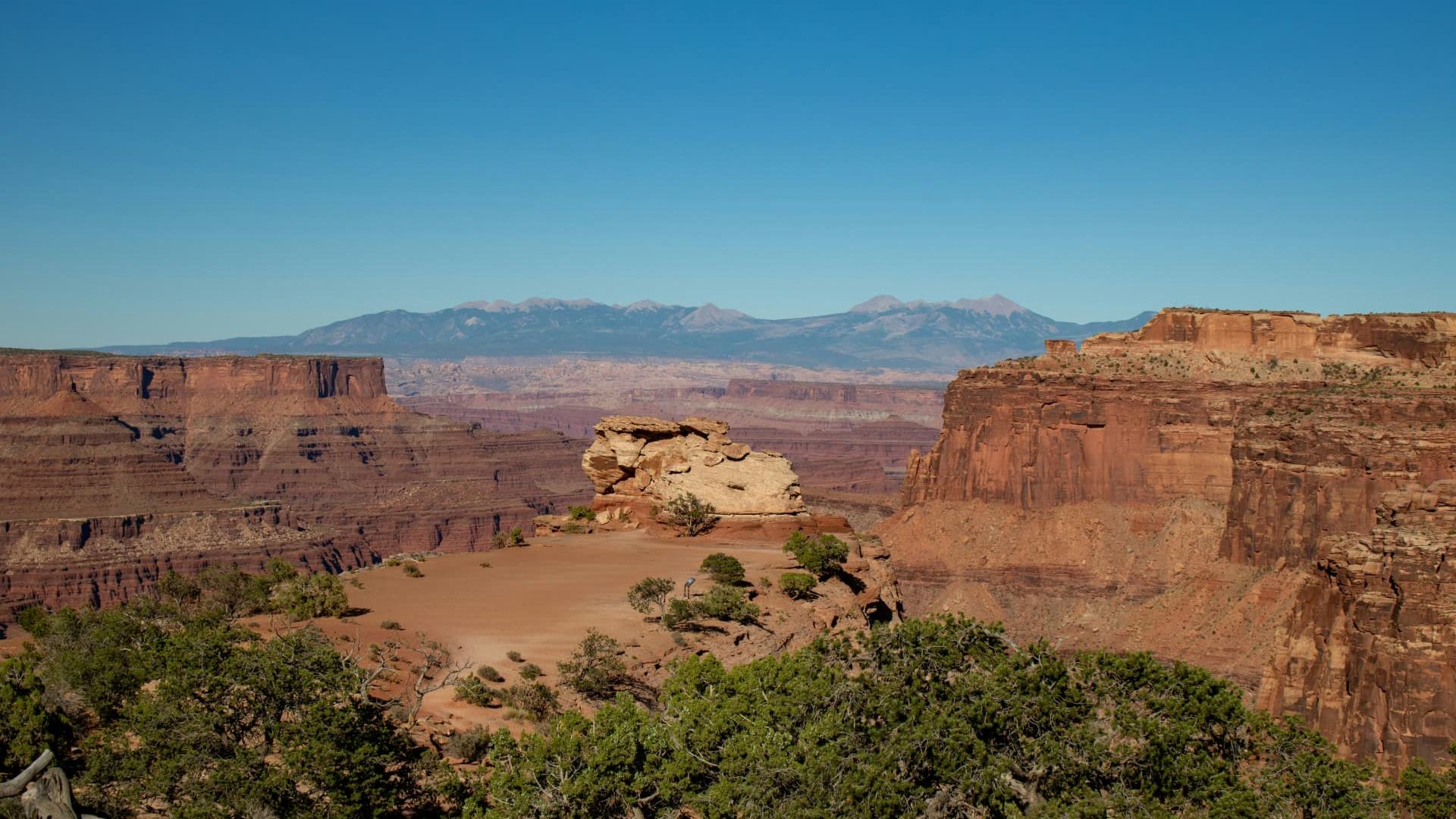 Red rock canyon rim and distant snow-topped peaks above the Hurricane Valley, Utah — ACA / Obamacare health insurance enrollment for 84737 households, Zion-corridor seasonal workers, and pre-Medicare early retirees