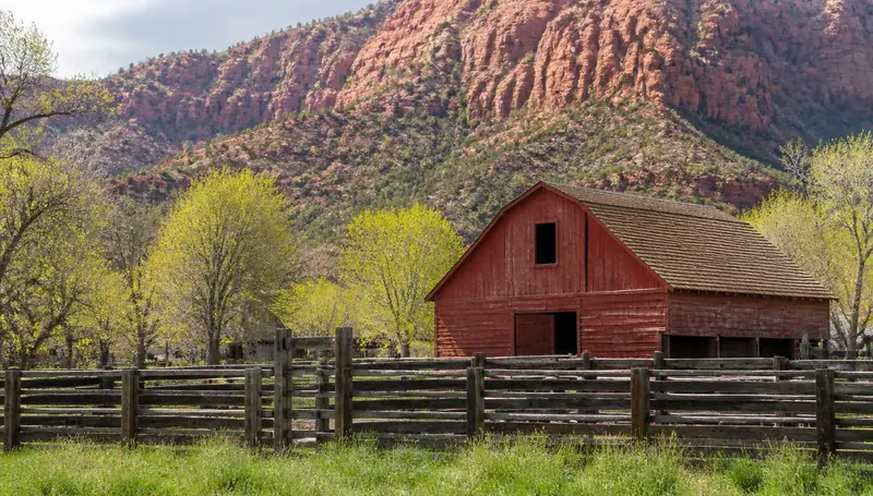 Old red barn and wooden corral below red rock mountains in Kanarraville, Utah — health insurance and ACA Marketplace enrollment for Kanarraville, Utah 84742 households