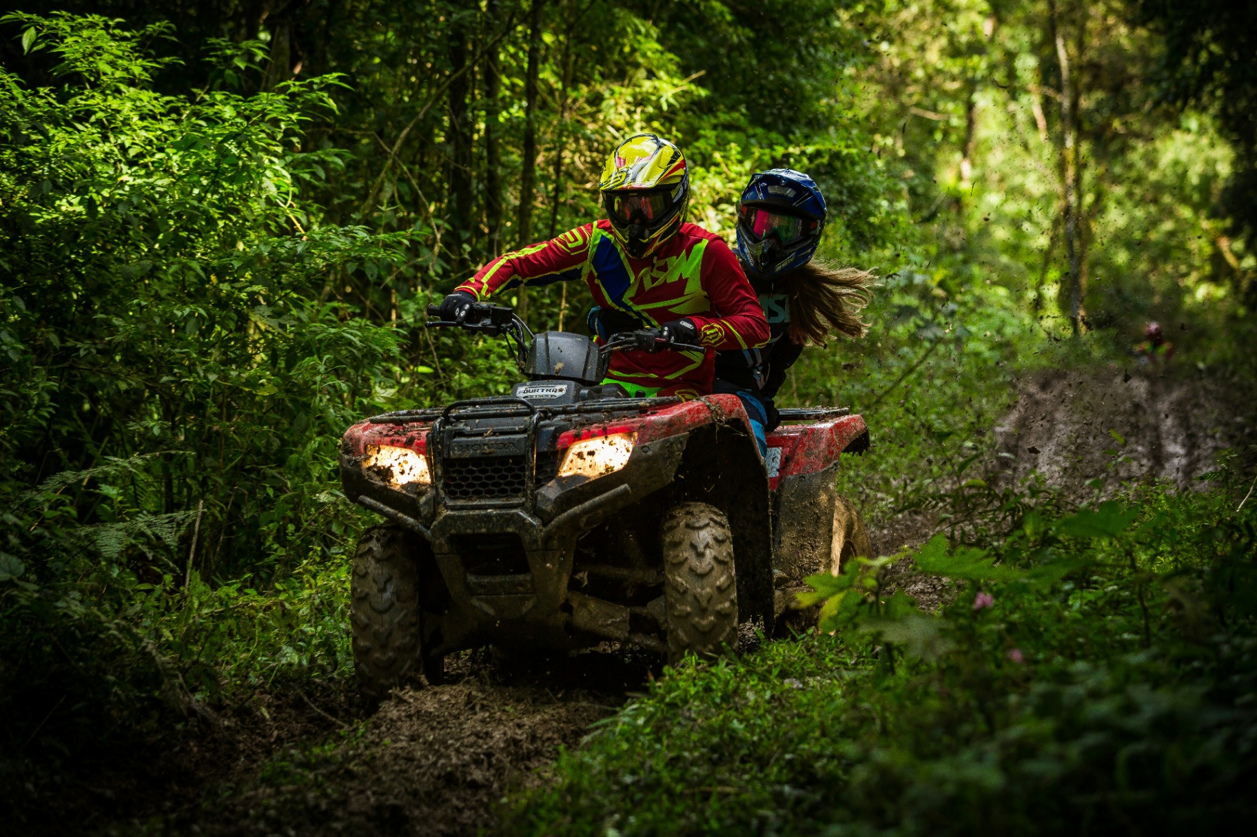 Two riders on a Honda Rancher ATV on a muddy trail — St. George ATV insurance with med-pay and guest passenger liability