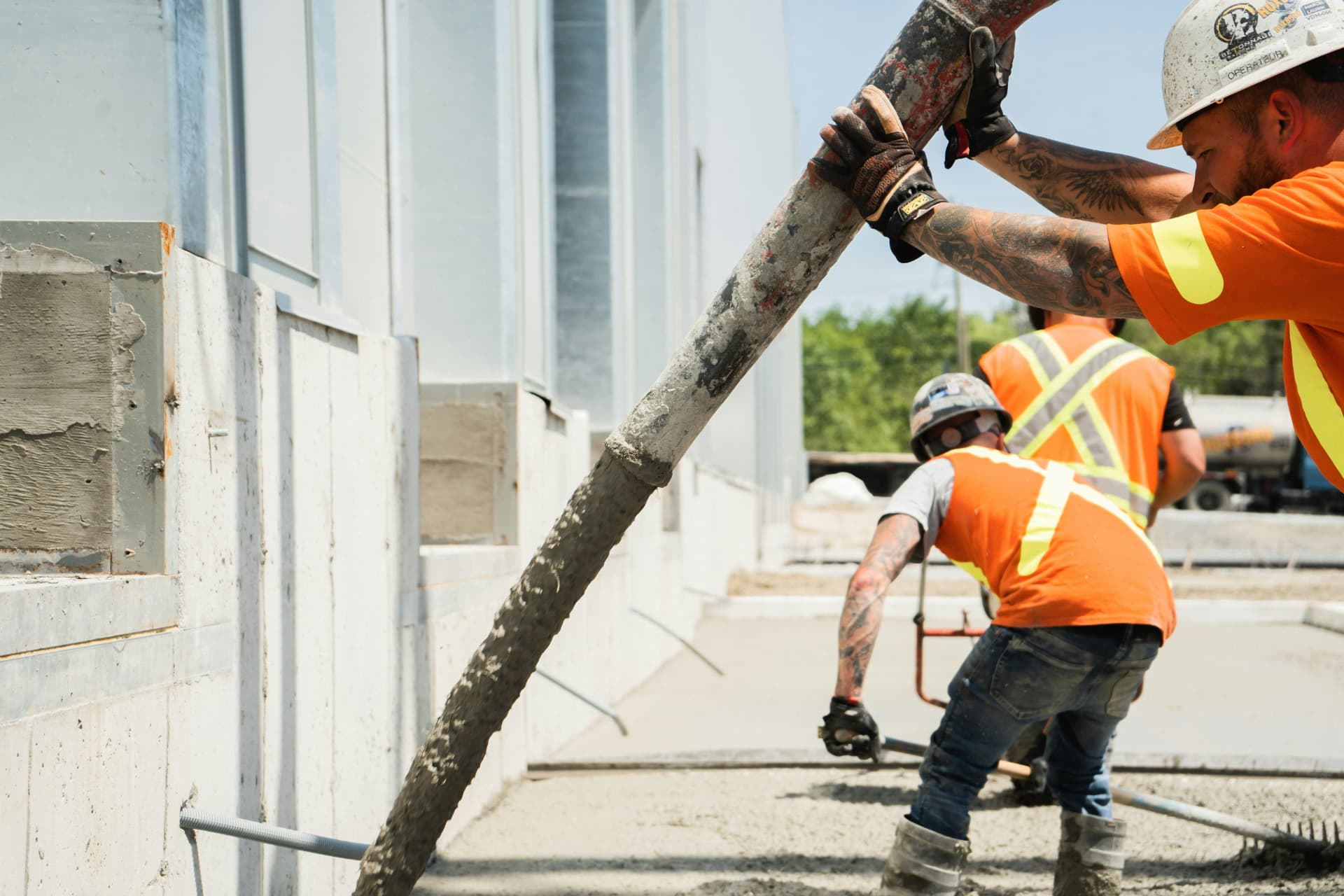 Construction crew in orange safety vests and hard hats pouring concrete from a pump hose on a St. George, Utah jobsite — general liability, workers' comp, and builders risk insurance for 84770 and 84790 contractors