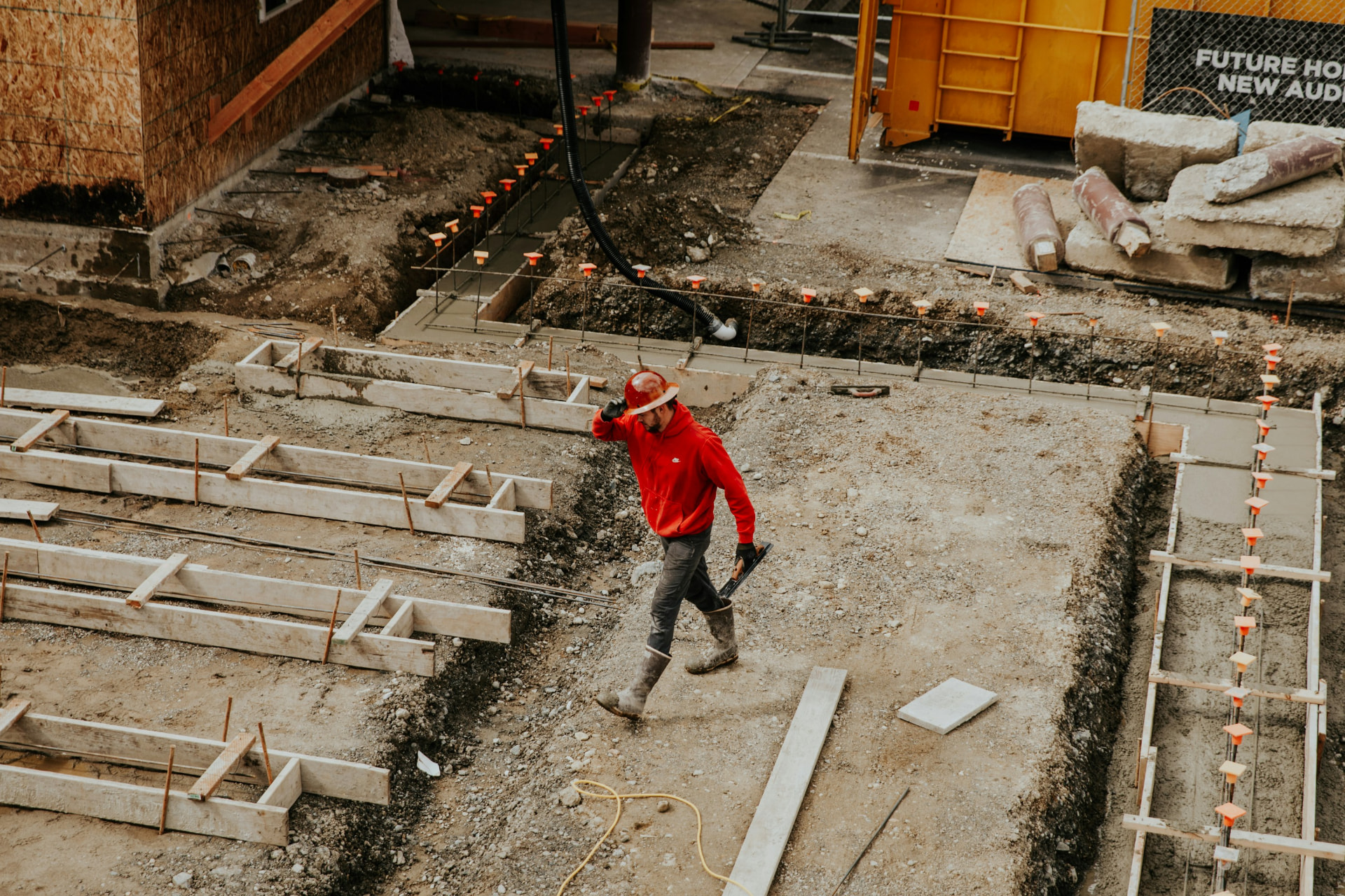 Construction worker in a red hoodie and hard hat walking a St. George, Utah jobsite foundation with wooden forms and rebar — contractors general liability, workers' comp, and builders risk for 84770 and 84790 trades