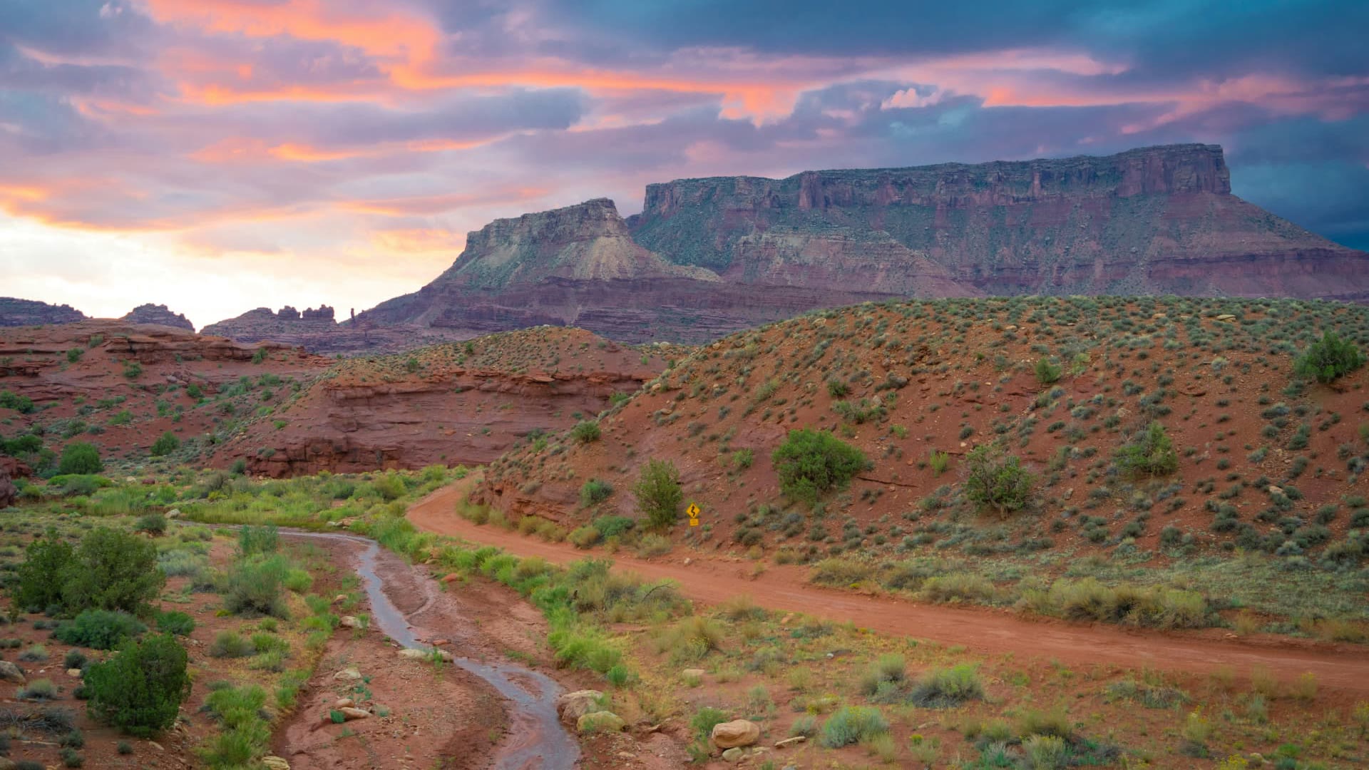 Red dirt road winding below a layered desert mesa at sunset near La Verkin, Utah — ACA / Obamacare health insurance enrollment for 84745 households, Confluence Park families, and self-employed St. George commuters