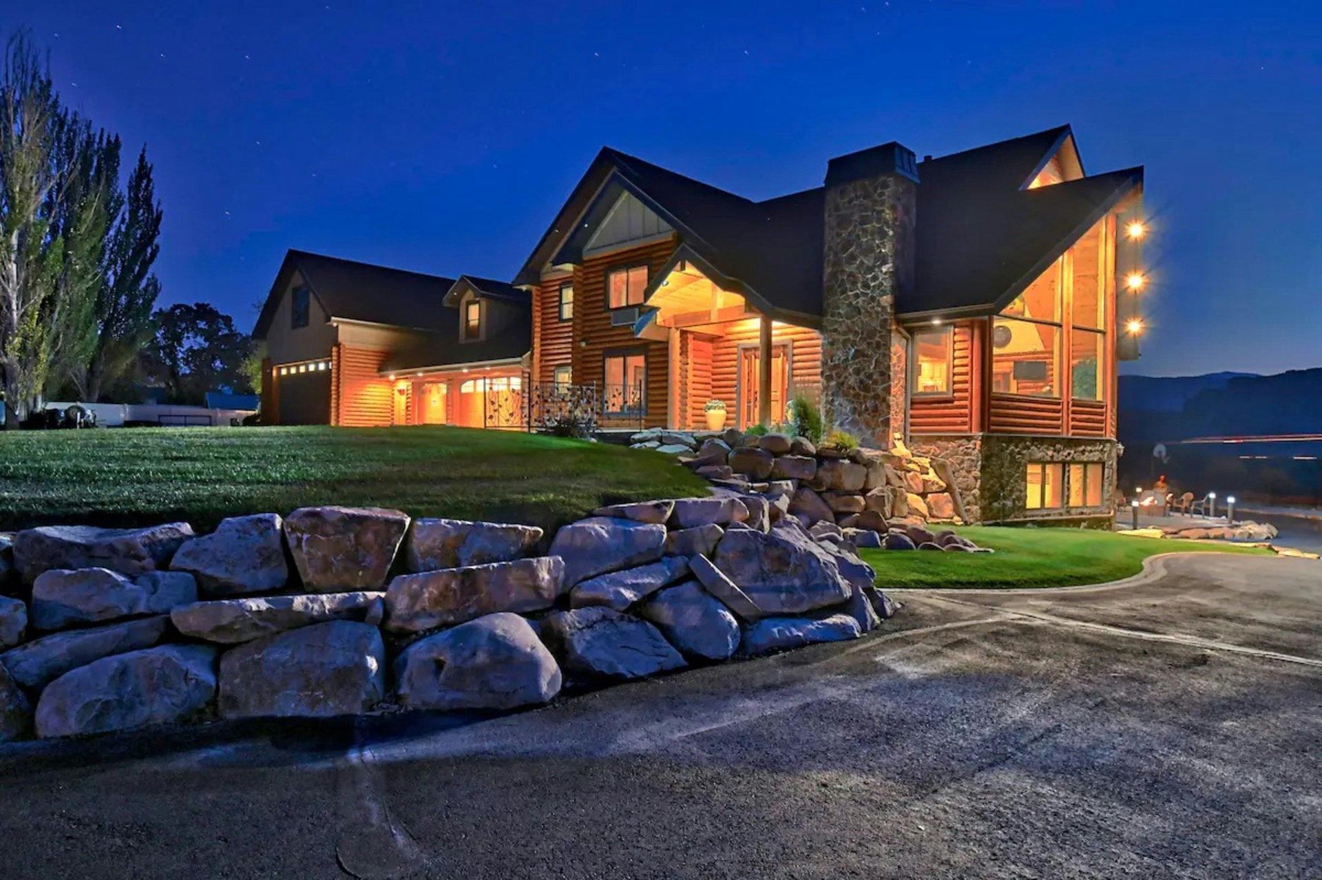 Large log-and-stone Pine Valley, Utah mountain home glowing warm at twilight with landscaped grounds and Pine Valley Mountain foothills behind — the higher-value custom mountain-home rebuild profile that carriers rate into every 84781 homeowners insurance quote