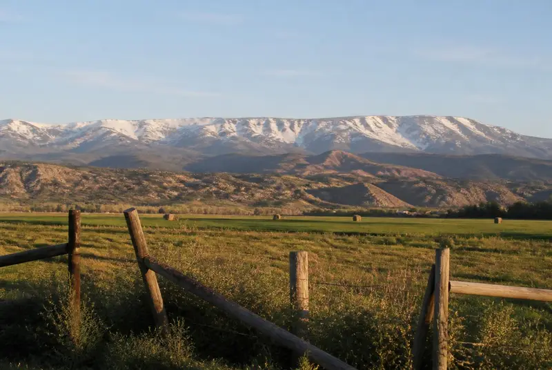 Irrigated alfalfa fields and a ranch fence in the Parowan Valley below the snow-dusted Markagunt Plateau — rural Iron County health insurance enrollment
