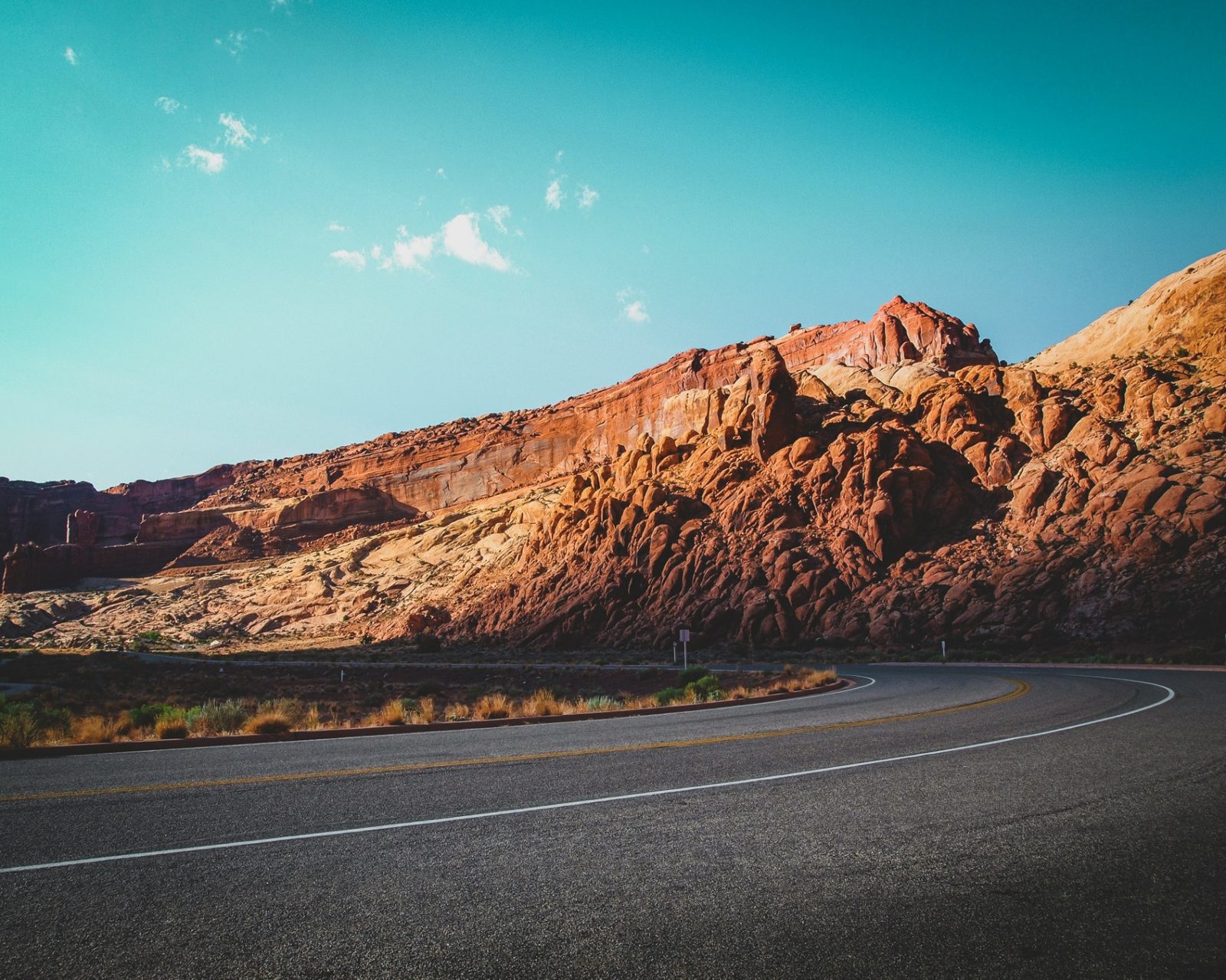 Old Highway 91 curving beneath red sandstone cliffs on the western edge of Santa Clara, Utah — the Snow Canyon wildland corridor and rebuild-cost profile carriers rate into every 84765 homeowners insurance quote