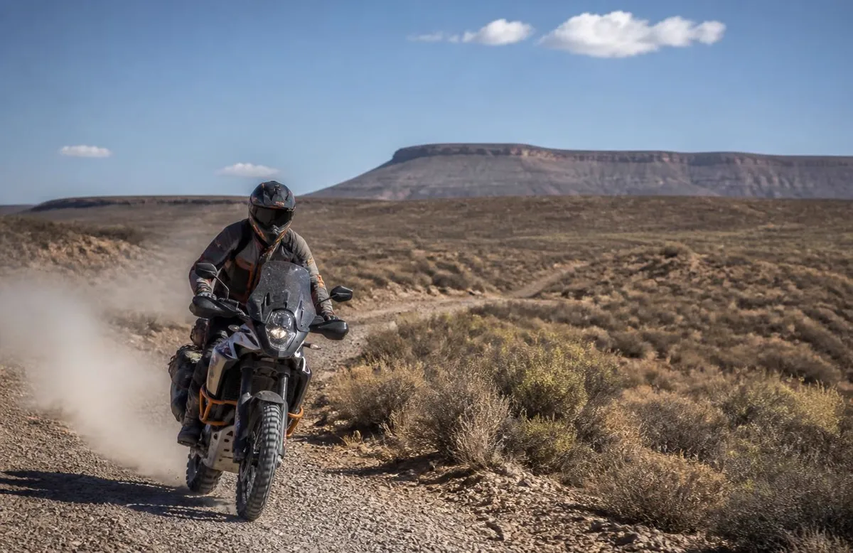 Dual-sport motorcycle raising dust on a high-desert gravel road outside Enoch