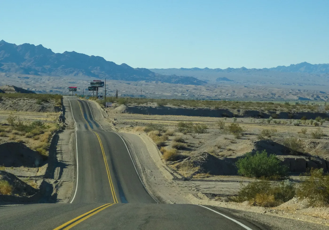 Desert road descending into the Mesquite, NV basin with the Virgin Mountains and Beaver Dam Wash corridor in the distance — the wildland-urban interface and monsoon-wind exposure carriers rate into every 89027 homeowners insurance quote
