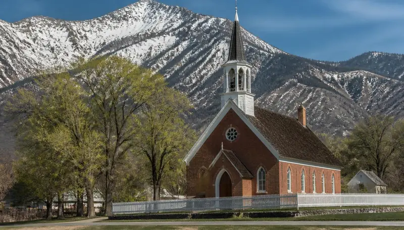 Red brick pioneer church below snow-capped mountains in Parowan, Utah — health insurance and ACA Marketplace enrollment for Parowan, Utah 84761 households