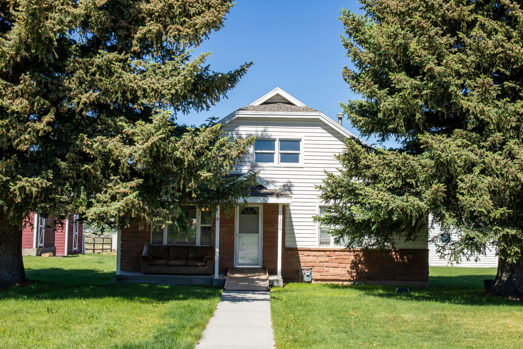 White-and-brick two-story rental home framed by mature spruce trees in Ivins, Utah