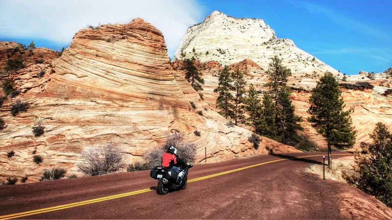 Motorcycle rider on the red asphalt of Zion–Mt. Carmel Highway with white Navajo sandstone domes above — OnPoint covers Southern Utah's national-park rides.