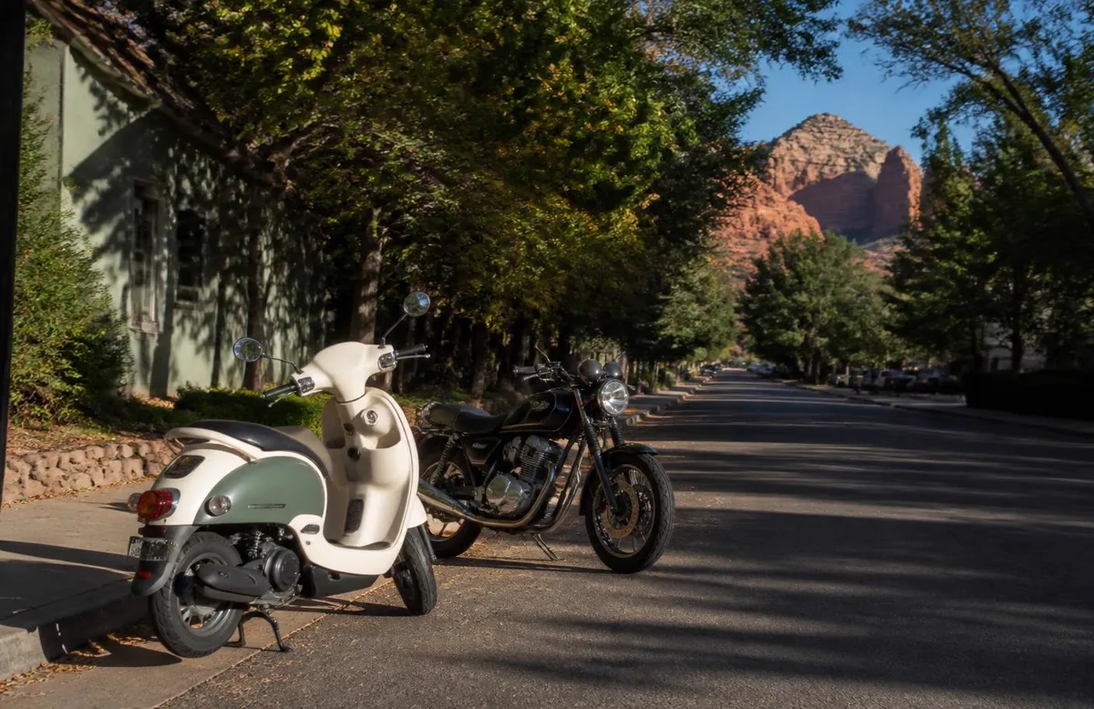 A scooter and a standard motorcycle parked on a shaded Salt Lake City side street
