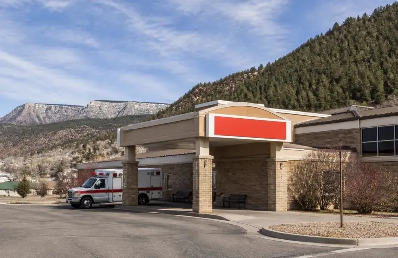 Small rural hospital with a covered emergency canopy and parked ambulance below pine-covered ridges — Garfield Memorial Hospital in Panguitch is the only hospital in Garfield County