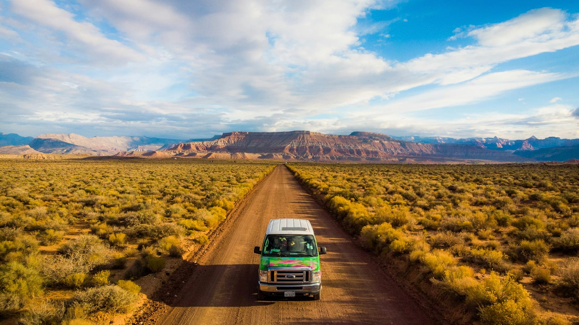 Camper van on a desert backroad outside Hurricane, Utah with mesas and red-rock cliffs on the horizon — auto insurance for Hurricane drivers