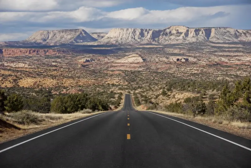 Empty two-lane highway running for miles across Grand Staircase-Escalante country toward white and red sandstone cliffs — distance and air-ambulance exposure shape Kane County health plans