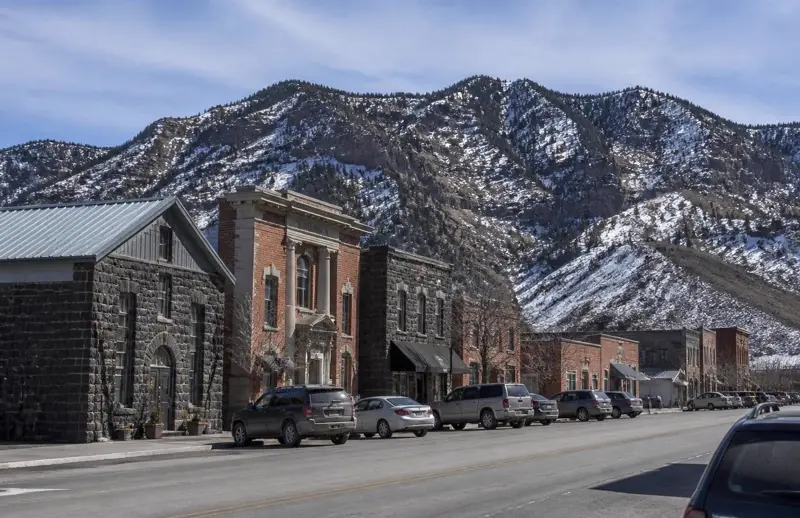 Historic black rock and brick buildings on Main Street in Beaver, Utah beneath the snow-streaked Tushar Mountains — free ACA health insurance enrollment for Beaver County households in 84713