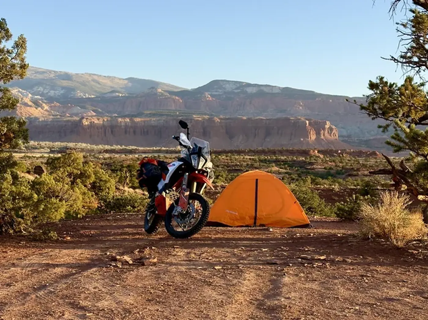 Adventure motorcycle and orange tent at a dispersed campsite near Capitol Reef red rock cliffs in Southern Utah
