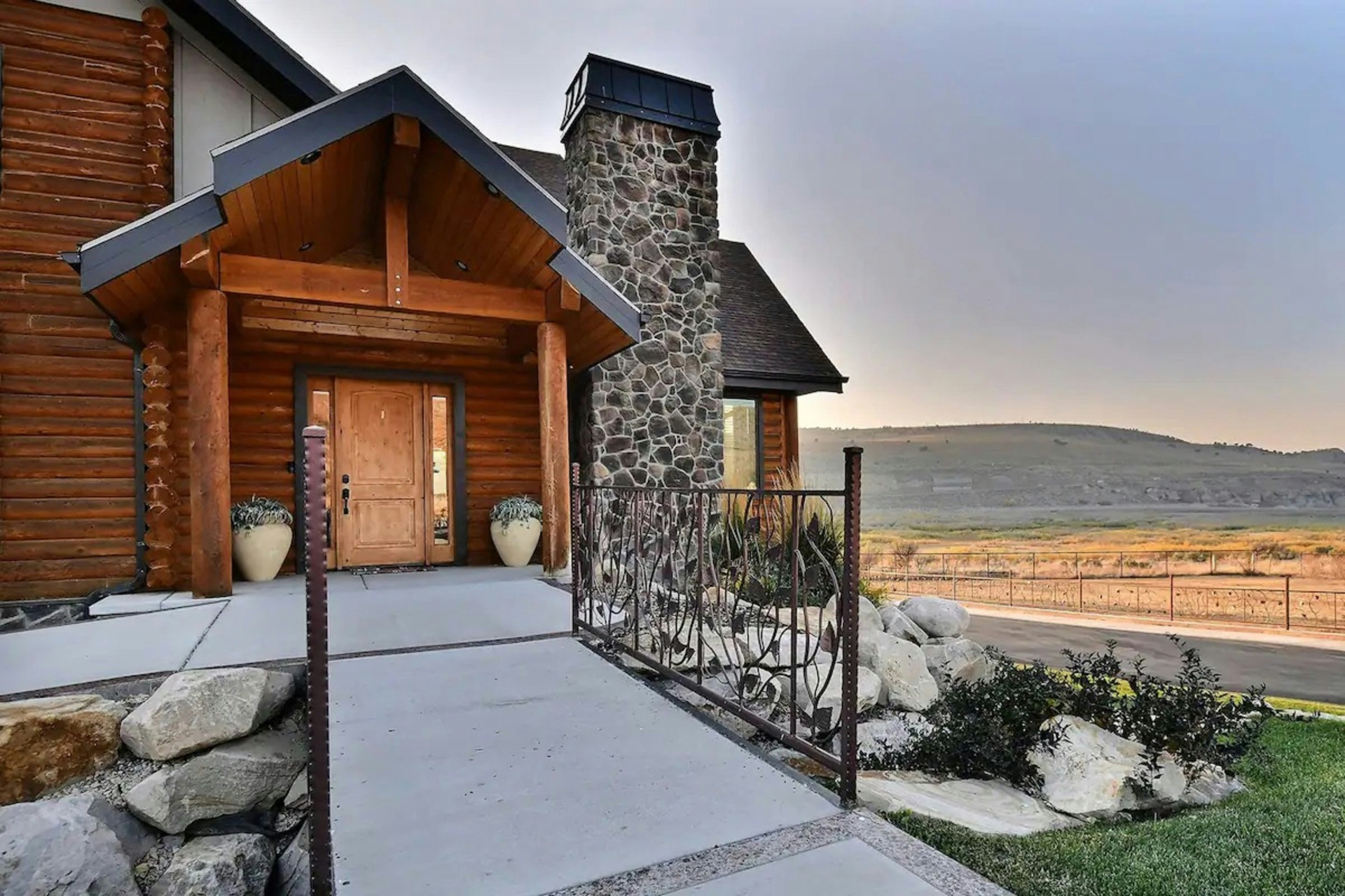 Log-and-stone entryway on a custom Enterprise, Utah ranch home at dusk with the Escalante Valley grasslands stretching to the horizon — the high-elevation ranching building style and outbuilding profile that shapes 84725 home insurance