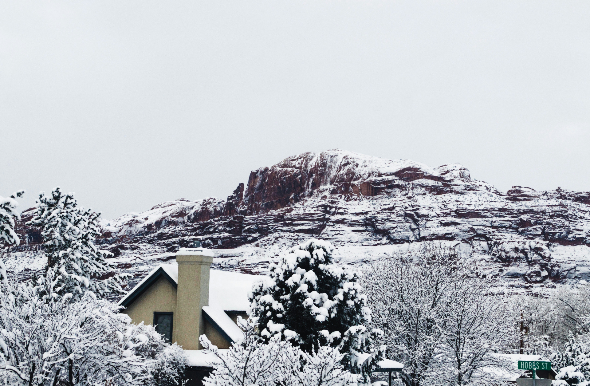 Snow-covered Pine Valley, Utah home with red sandstone cliffs rising behind snowy pines — the 6,700 ft snow-load, freeze-burst pipe risk, and Pine Valley Mountain WUI edge that carriers rate into every 84781 homeowners insurance quote