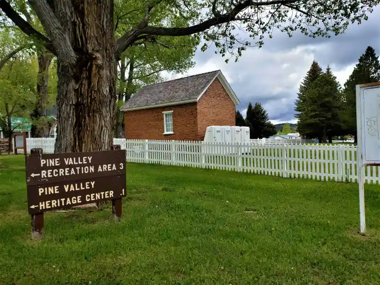 Pine Valley Recreation Area and Heritage Center directional sign beside a brick pioneer building and white picket fence — 84781 Pine Valley, UT
