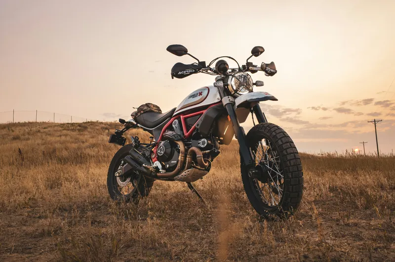 Ducati Scrambler with custom parts parked in golden Utah grassland at sunset — the kind of build OnPoint schedules custom-parts coverage for.