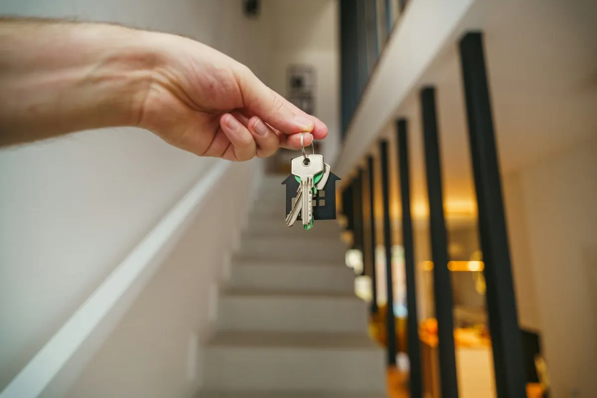 Landlord handing over house keys on a house-shaped keychain in a rental entryway