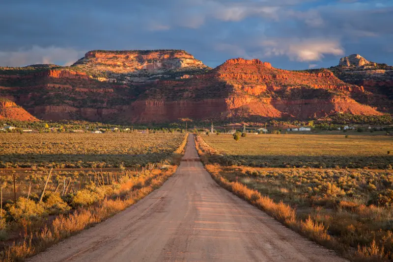 Red Vermillion Cliffs at sunset above a dirt road outside Kanab, Utah — the kind of remote Kane County terrain that drives auto-insurance tow-distance and comprehensive-coverage decisions
