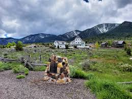 Carved wooden stump with farmhouse and snow-dusted Pine Valley Mountain behind — the 84781 mountain community OnPoint writes auto insurance for