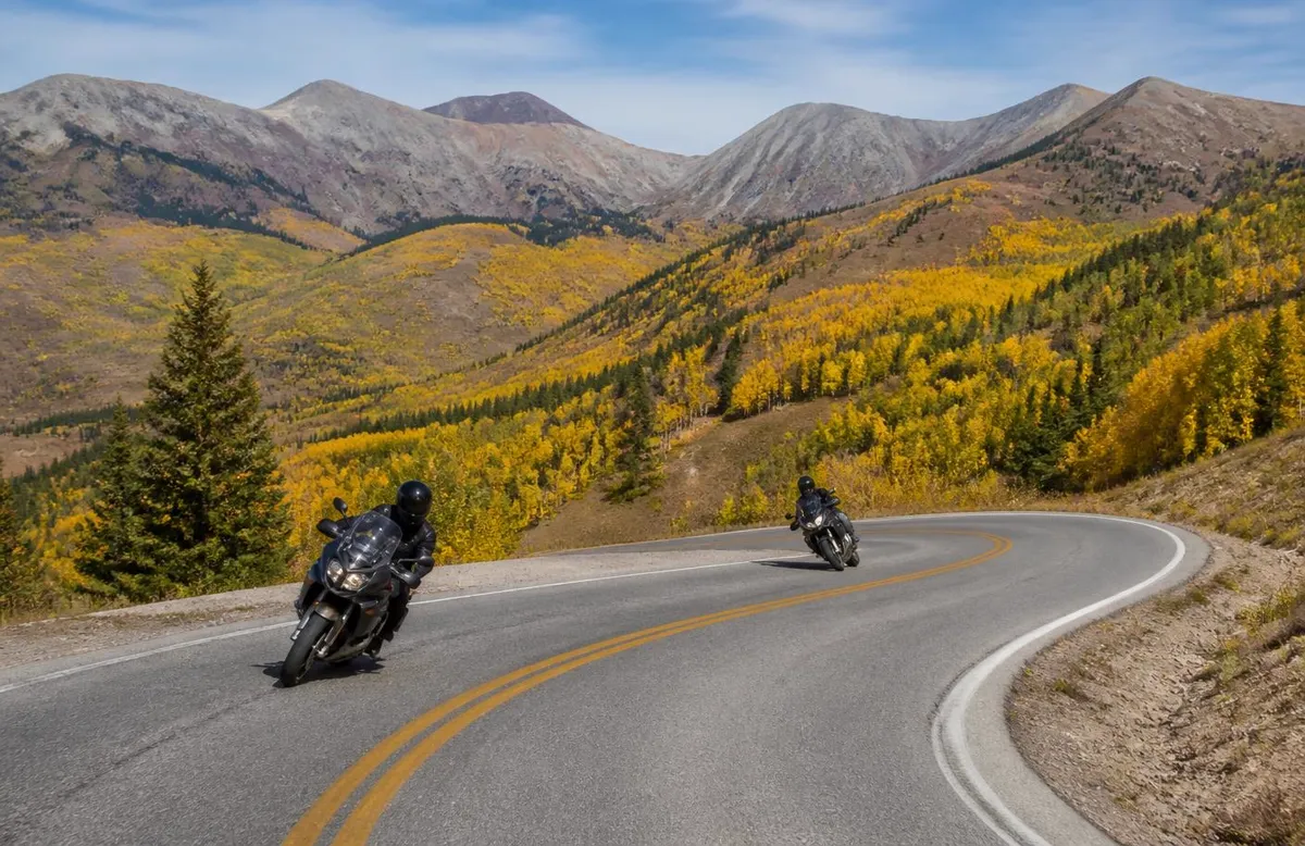 Two motorcycles leaning through mountain switchbacks in autumn aspens above Salt Lake City
