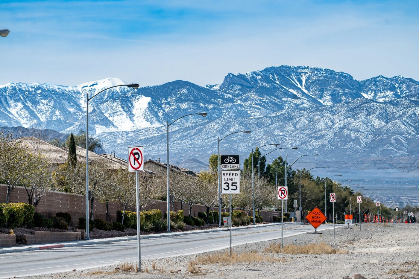 Snow-capped Virgin Mountains rising over a Sun City Mesquite neighborhood along a landscaped 89027 boulevard — the tile-roof, monsoon-wind, and wildland-urban interface exposure that shapes Mesquite, NV homeowners insurance