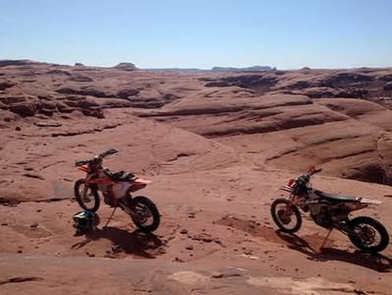 Two dirt bikes parked on Moab slickrock with Utah desert buttes in the distance — OnPoint covers off-road and dual-sport riders statewide.