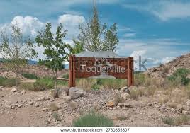 Carved wooden Toquerville, Utah town entrance sign on basalt boulders along SR-17 with cottonwoods and the Pine Valley Mountains behind — the 84774 town limits OnPoint quotes auto policies for