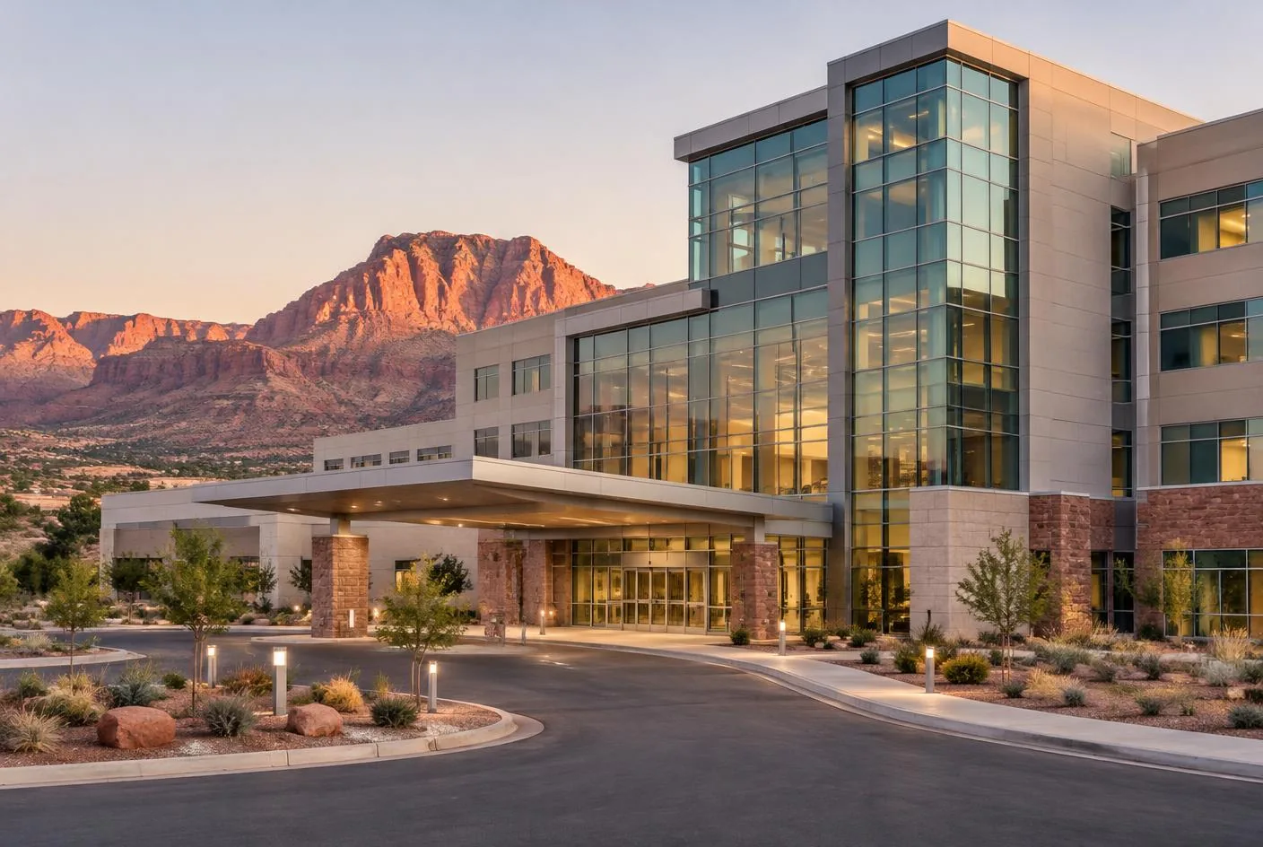 Regional hospital tower at dusk with a covered entrance and red rock bluffs behind it in Southern Utah