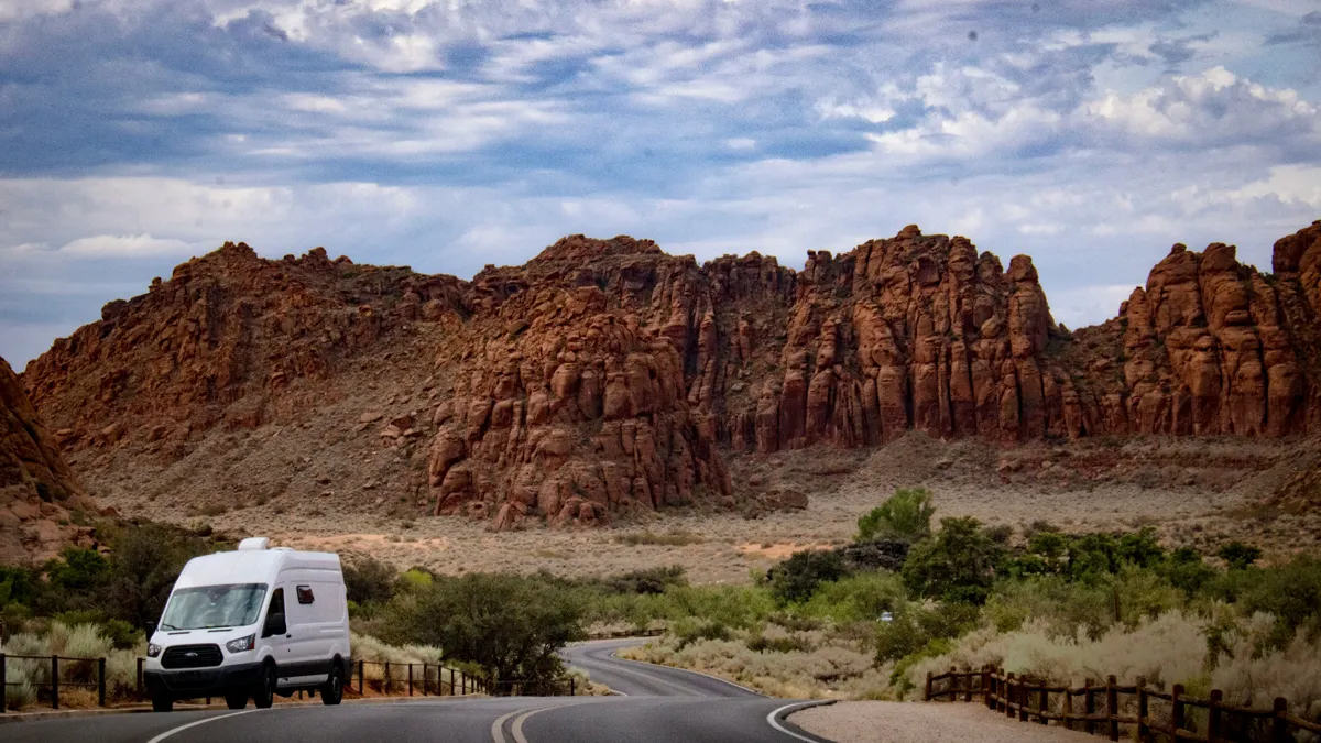 Camper van driving past red sandstone cliffs in Snow Canyon State Park near St. George, Utah
